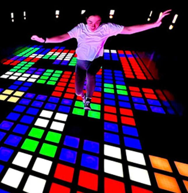 A player reaching for a scoring tile on the Super Grid LED floor